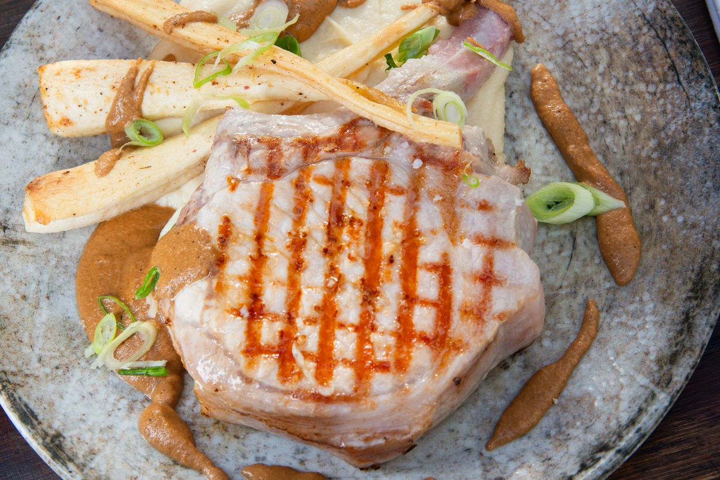 Côte de porc grillée, sauce noisette, panais rôtis et oignons nouveaux dans une assiette en grès bleu