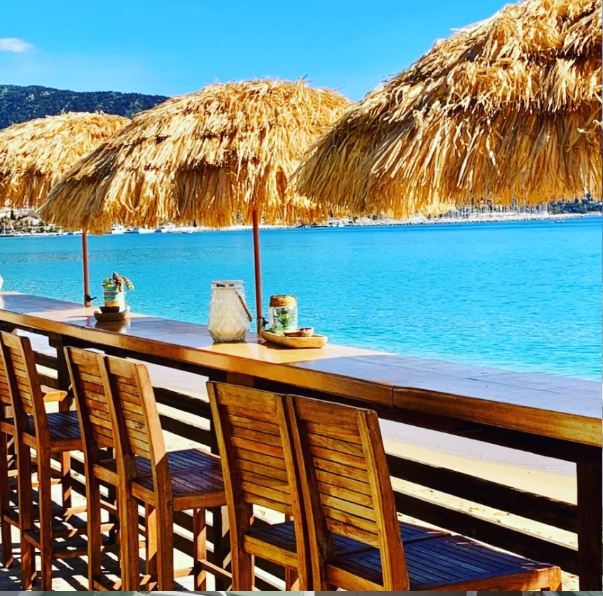 Le bar de L'Effet Mer, tabourets en bois face à l'eau turquoise sous les paillotes en paille