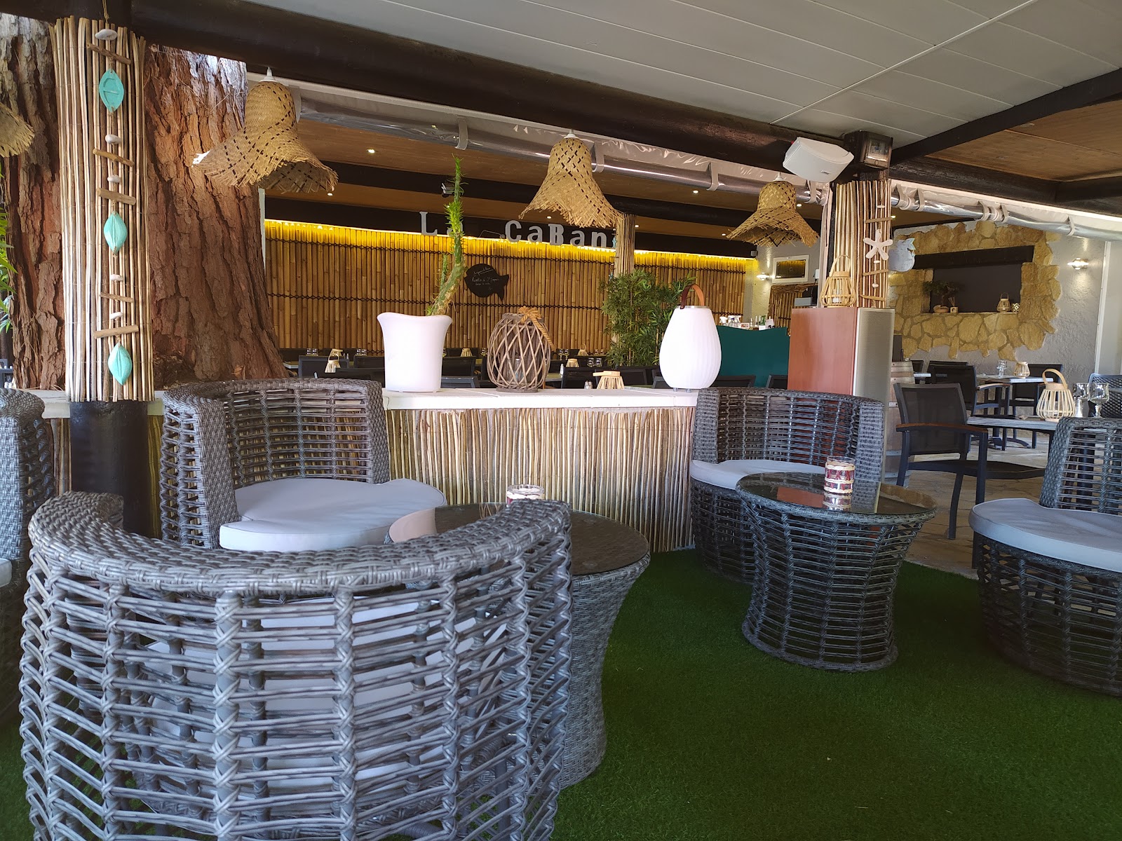 Le bar-lounge de La Cabane : fauteuils en rotin, comptoir en bambou et suspensions en paille sous la pergola