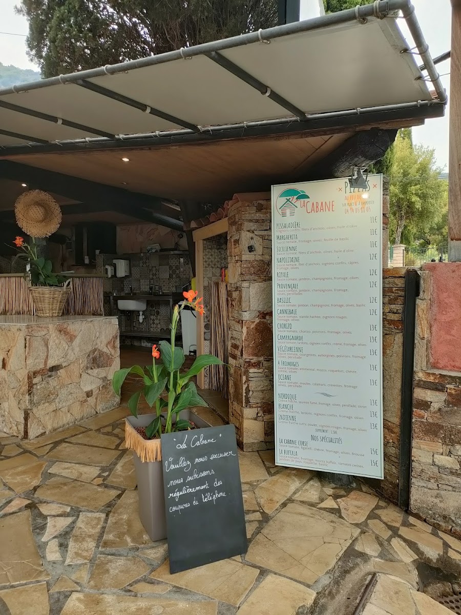 L'entrée rustique de La Cabane : mur en pierre sèche, chapeaux de paille et ardoise du jour