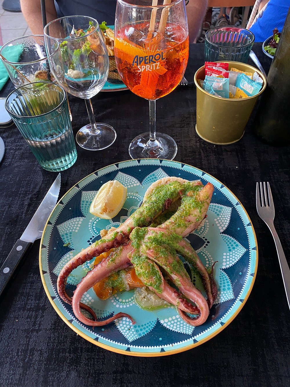 Poulpe grillé au pesto sur assiette turquoise, avec un Aperol Spritz