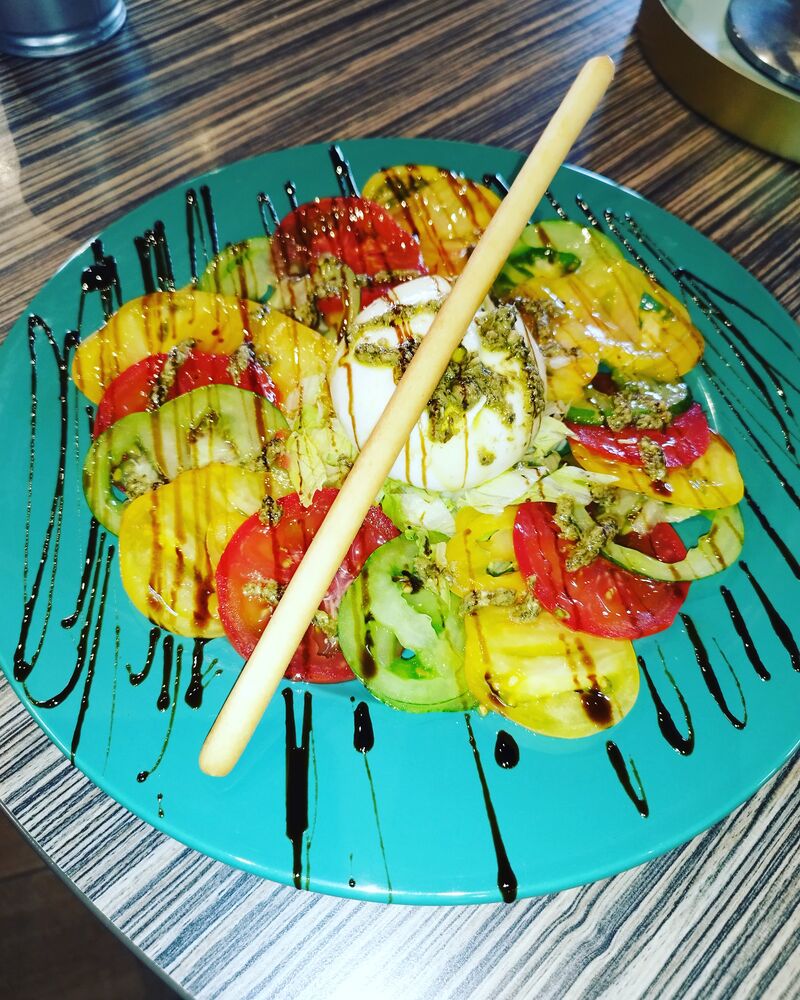 Plat signature mozzarella burrata et tomates multicolores dans une assiette turquoise