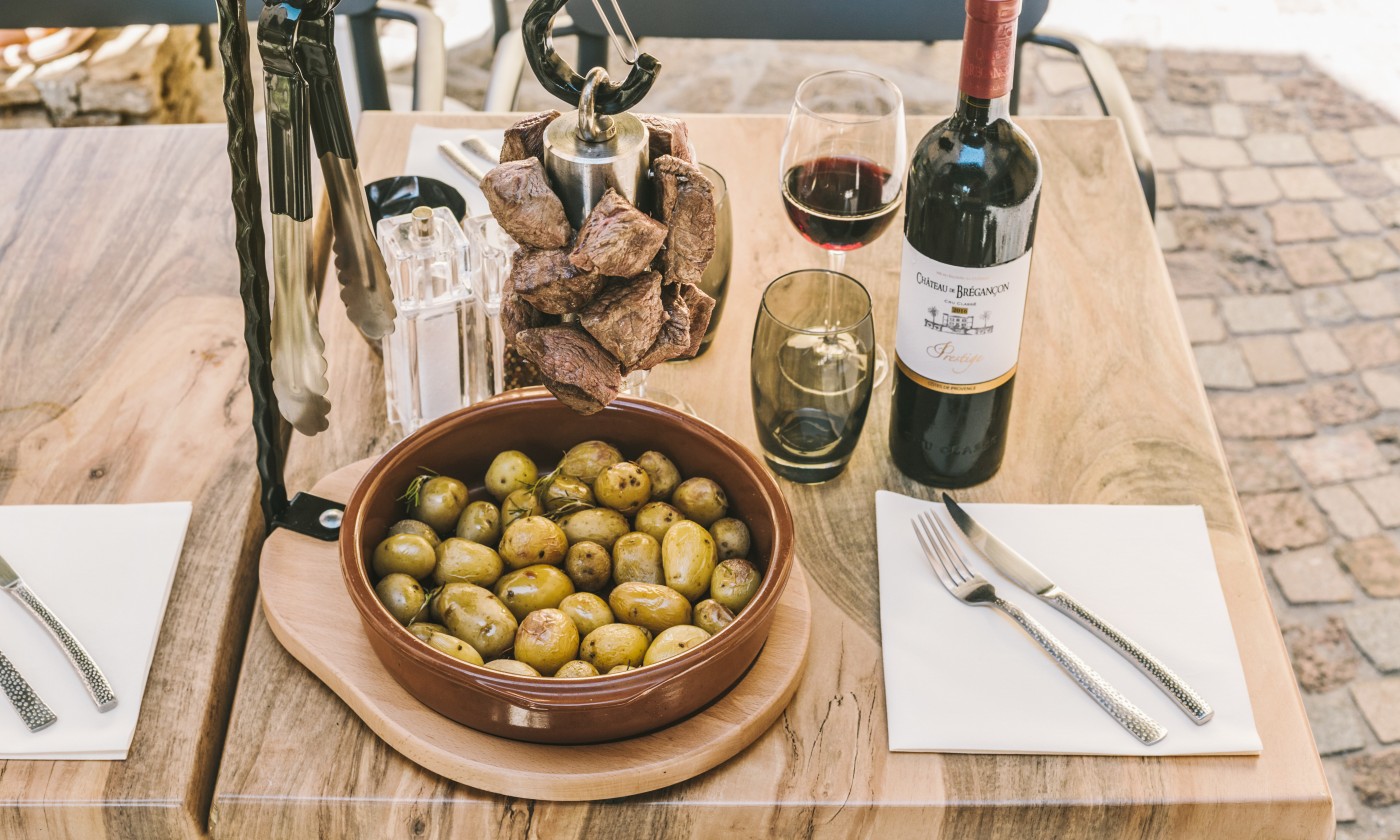La potence flambée de L'Emberluque : cubes de bœuf saisis, suspendus à la potence, servis avec des pommes grenaille au romarin et un verre de rouge de Provence