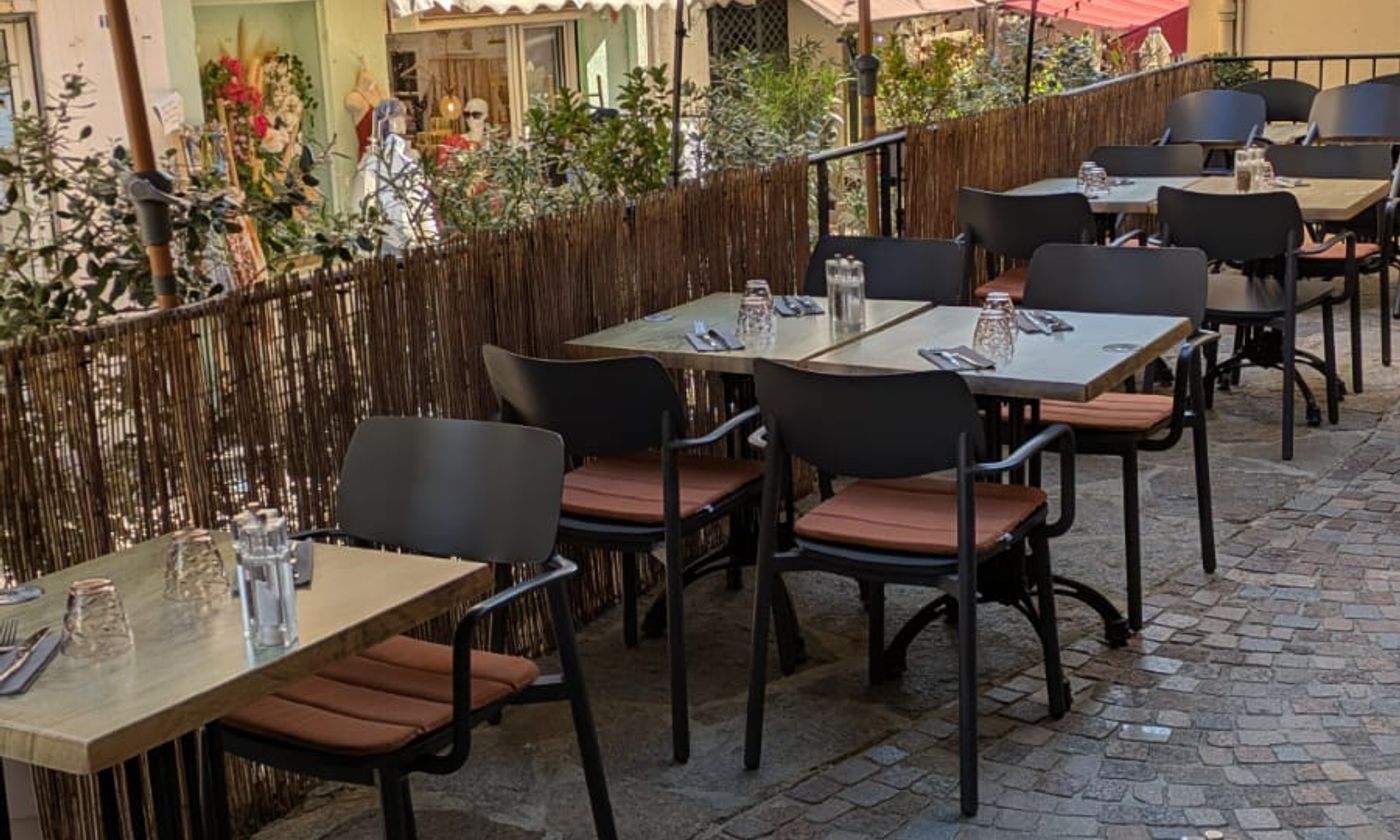 La terrasse de L'Emberluque installée dans la ruelle pavée du Lavandou, tables en bois et plantes le long d'une palissade en roseau