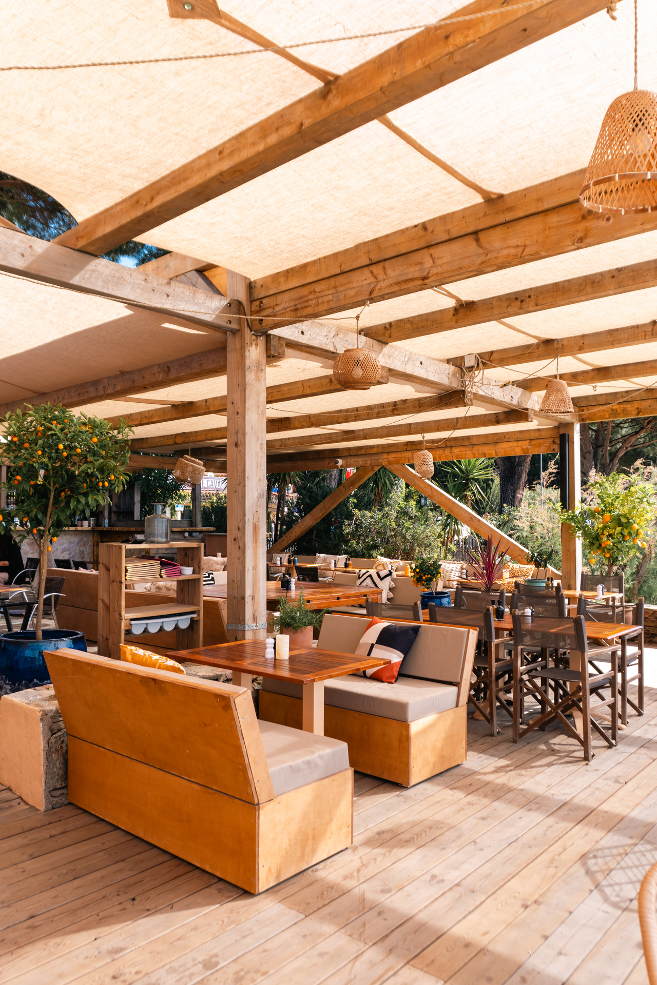 Coin lounge de Noca Plage bordé d'agrumes, banquettes en bois et lanternes tressées sous les voiles