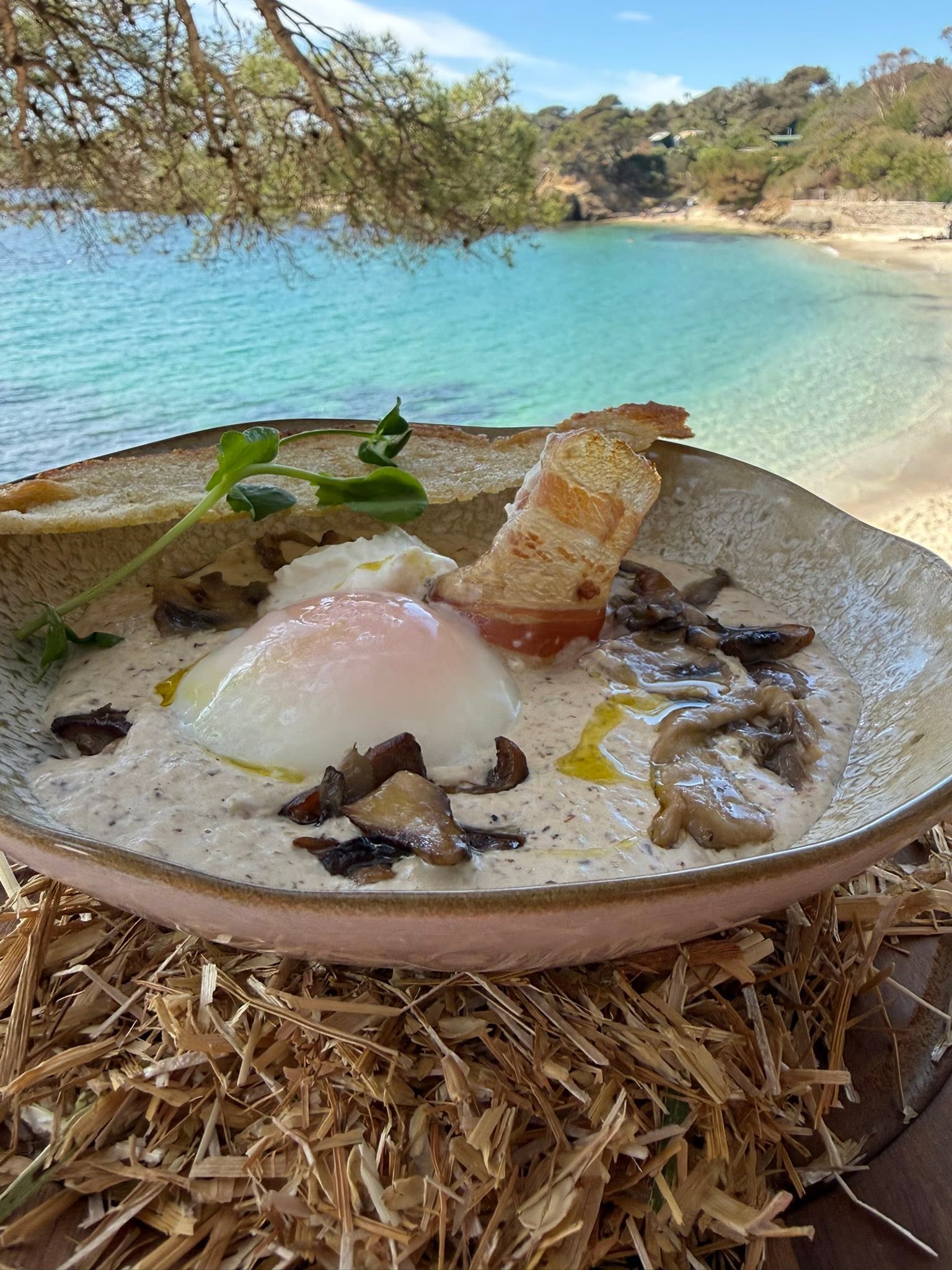 Œuf parfait, crème de champignons et lard croustillant, servi face à l'eau turquoise de la crique